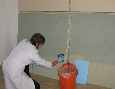 IGERT Trainee Brent Stephens is applying a clay-based wall covering to gypsum wallboard for full-scale testing in an NSF-funded test house (UTest House)
